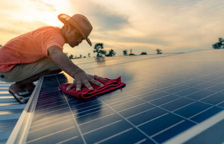 Man cleaning solar panel on roof. Solar panel or photovoltaic module maintenance. Sustainable resource and renewable energy for go green concept.  Solar power for green energy. Technology for future.の写真素材