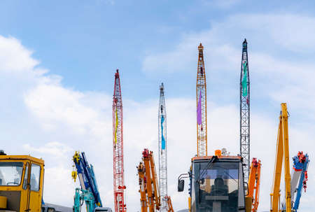Close-up mobile crane, yellow bulldozer, and blue backhoe parked at second-hand machinery auction yard against blue sky. Heavy machinery for rent and sale. Crane dealership for construction business.の写真素材