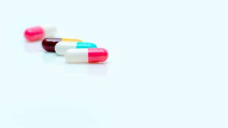 Selective focus on antibiotic capsule pill. Pharmaceutical industry. Prescription drugs. Pharmacy web banner. Pink, blue, yellow, red capsules pill on white background. Antibiotic drug resistance.の写真素材
