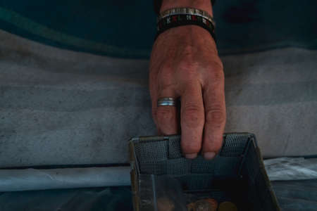 Homeless hand with small basket with coin on the street. Beggar begging for money. Poor man sit on...