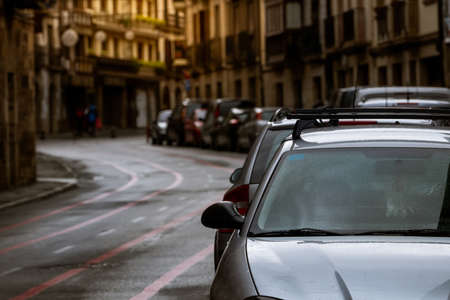 Row of cars parked along the street and old buildings in Europe city. Many cars parked on road in old town. City street in Europe. Front view of car parked outside residential building. City traffic.の写真素材