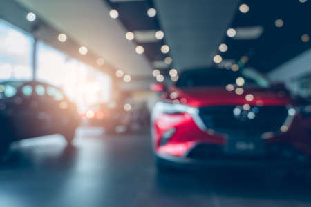 Blurred photo new red car parked in showroom. Car dealership office. Car parked in showroom with care. Car for sale and rent business. Automobile leasing market. Electric vehicle. Automotive industry.の写真素材