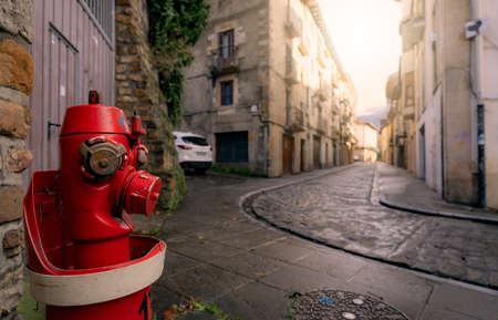Red fire hydrant on sidewalk in Onati city, Spain. Fire hydrant on blur old building, white car, and street. Cityscape. Water supply for fire extinguisher. Fire control system of the city for safety.の写真素材