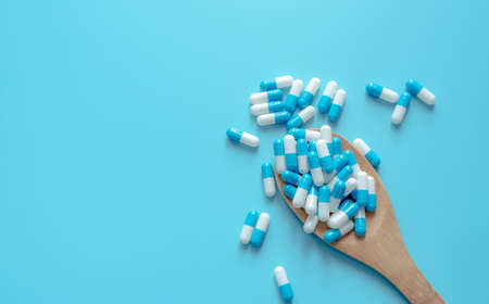 Blue-white capsule pills on wooden spoon. Capsule pills on blue background. Health topics. Drug for...