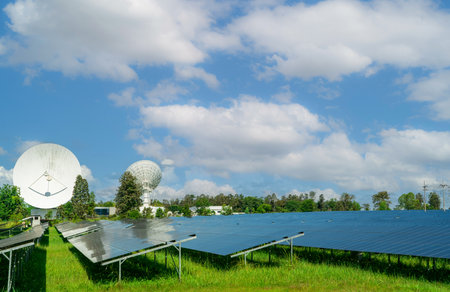 Solar farm and green field with blue sky. Big satellite dish near solar farm. Solar power for green...