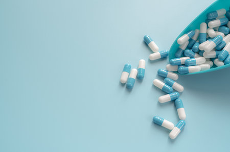Blue and white capsules pill in plastic spoon and on blue background. Antibiotics drug resistance....