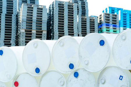 Old chemical barrels. Empty white chemical drums stack on blur industrial plastic pallets. Toxic waste warehouse. Hazard chemical barrel. Industrial waste in drum. Hazard waste storage in factory.の写真素材