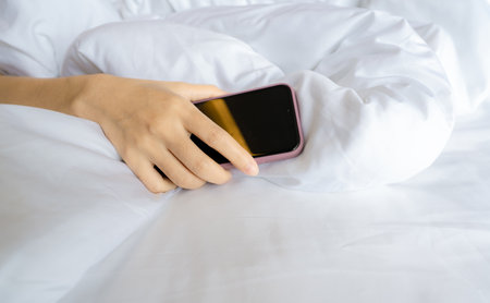 Woman sleeping in bed and hand holding mobile phone. Woman using smartphone in bedroom. Asleep with smartphone. Work life imbalance. Unhealthy sleeping. Social media addict. Need social detox concept.の写真素材