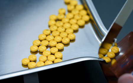Selective focus on yellow tablets pills on stainless tray with blur hand of pharmacist or pharmacy technician counting pills into a plastic zipper bag. Prescription medicine. Medical health care.の写真素材