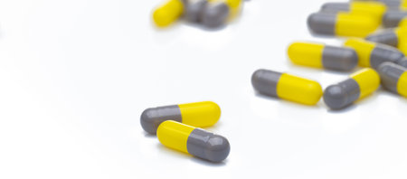 Closeup yellow and gray capsule pills on white background. Prescription drugs. Pharmaceutical industry. Health and medical care concept. Pharmacy products. Capsule pills production manufacturing.の写真素材