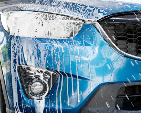 Blue car wash with white soap foam. Auto care business. Car cleaning service. Vehicle cleaning service. Foam wash car detailing. Headlamp light of the blue luxury SUV car is covered with white foam.の写真素材