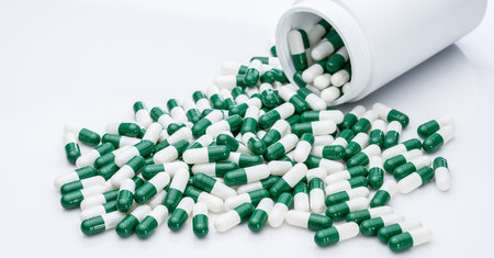Green and white capsule pills spilled out of a white plastic bottle. Pharmaceutical industry. Prescription drug. Healthcare and medicine. Pharmacy product. Pharmaceutics. Capsule pill manufacture.の写真素材