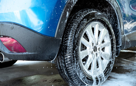 Blue car wash with white soap foam and professional auto care service. Car cleaning service concept. Vehicle cleaning service. Foam wash car detailing. Tire of car wheel is covered with white foam.の写真素材