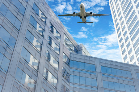 Airplane flying in the sky above modern sustainable glass office building. Exterior skyscraper green glass building. Business travel. Aviation business. Air logistics. Cargo plane. Departure flight.の写真素材