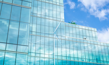 Green corporate building with wind turbine shadow cast on glass facade. Sustainable energy and efficient architectural design. Eco-friendly and modern urban development. Sustainable economic growth.の写真素材