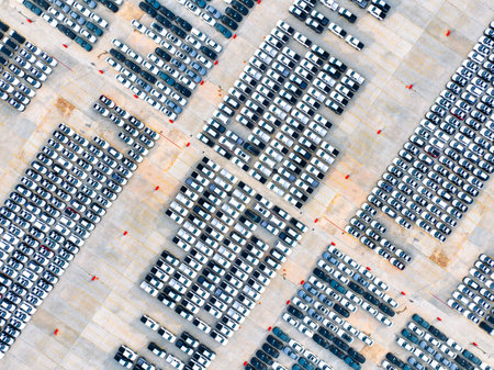 Aerial view of automotive logistics. Factory parking lot filled with rows of new cars. Modern...