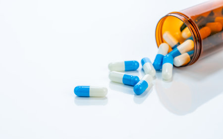 Prescription antibiotic capsules spilling from amber bottle onto a white background. Blue and white capsule pills. Ideal for healthcare, pharmaceutical treatments, and medical medication industries.の写真素材