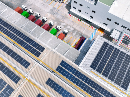 Solar-powered warehouse facility with freight trucks at loading docks. Eco-friendly logistics and efficient cargo transportation. Solar panels and sustainable energy concept in distribution center.の写真素材