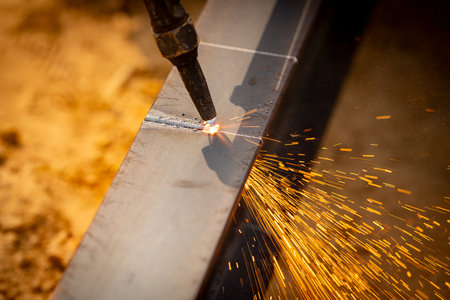 Skilled welder cuts metal with a gas torch in industrial workshop. Sparks fly during precision...