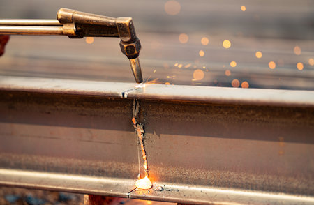 Welder using gas torch to cut metal beam, with sparks flying. Skilled craftsmanship and risks...