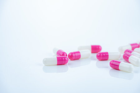 Pink-white antibiotic capsules spread on white background. Prescription drug. Antibiotic resistance in modern medicine. Healthcare and pharmaceutical industry. Medical care, pharmaceutical research.の写真素材