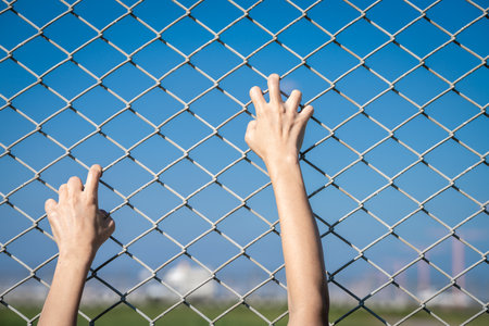 Closeup of a human hand gripping a chain link fence as if trying to escape, representing border...