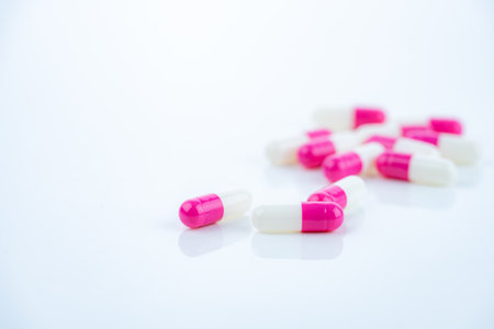 Pink-white antibiotic capsules spread on white background. Prescription drug. Antibiotic resistance in modern medicine. Healthcare and pharmaceutical industry. Medical care, pharmaceutical research.の写真素材