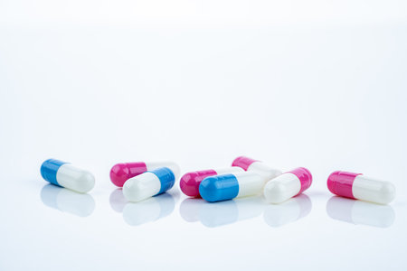Blue and pink capsule pills spread on white background, showcasing pharmaceutical products,...