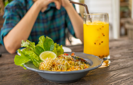 Seafood pasta plate served with green salad and lime wedge alongside tropical passion fruit juice on casual restaurant table. Person enjoying Mediterranean meal. Cuisine and relaxation meet in summer.の写真素材