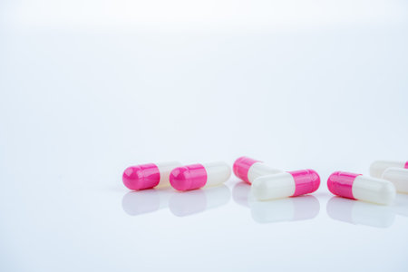 Pink-white antibiotic capsules spread on white background. Prescription drug. Antibiotic resistance in modern medicine. Healthcare and pharmaceutical industry. Medical care, pharmaceutical research.の写真素材