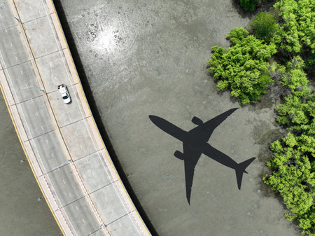 Airplane shadow flying over mangrove forest with car driving on coastal concrete bridge. Sustainable aviation biofuel technology. Environmental conservation. Eco-friendly flight. Mangroves capture CO2の写真素材