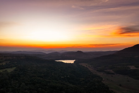 Beautiful orange sunrise over mountain range and lake from aerial view showcasing natural landscape and watershed forest sustainability concept for environmental conservation and tourism marketingの写真素材