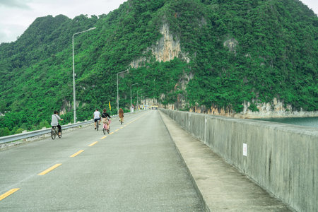 Family cycling together along a concrete road on a scenic dam surrounded by limestone cliffs during...
