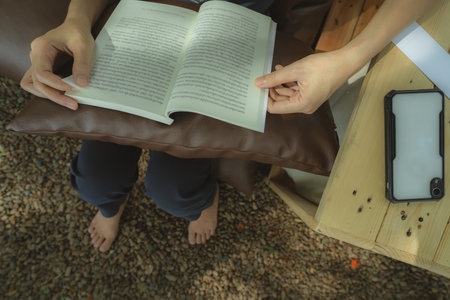 Woman enjoying digital detox weekend retreat while reading book on outdoor hotel seating with bare...