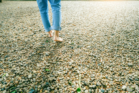 Close-up of barefoot woman walking on gravel ground in a peaceful forest retreat during early morning light. Self-care, emotional healing, and connection with nature for mental balance. Mindfulness.の写真素材