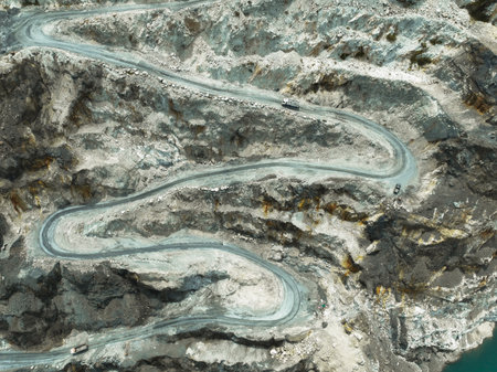 Drone shot capturing heavy machinery moving through terraced quarry levels in a limestone mine,...