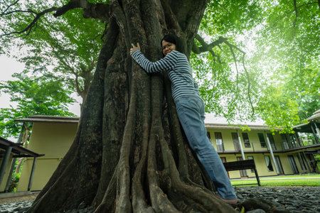 Asian woman hugging big tree trunk. Eco retreat. Nature connection therapy for mental health wellness and digital detox healing in natural environment. Mental wellness and digital detox at eco hotel.の写真素材