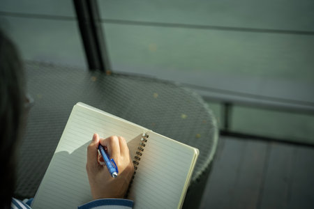Close-up of woman's hand writing in notebook outdoors. Self-reflection, goal setting, journaling habit, and mindful planning. Creativity, life planning, and focus on personal growth. Mindful practice.の写真素材