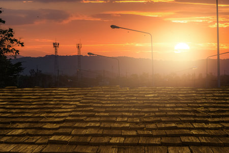 Wooden roof tiles glowing under warm sunlight during sunset with hills in background. Natural texture, architectural detail, and peaceful countryside evening atmosphere.の写真素材