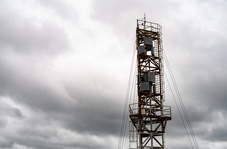 Steel wind measurement tower with mounted sensors standing beside reservoir under cloudy sky in wind farm field. Renewable energy research, environmental monitoring, and sustainable development.の写真素材