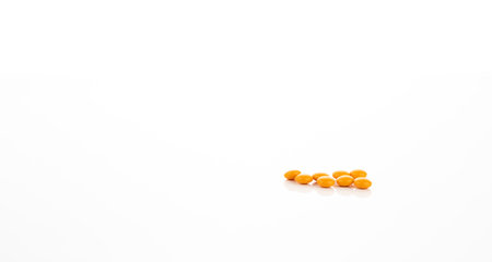 Prescription medicine yellow sugar coated tablet pills on white background representing...