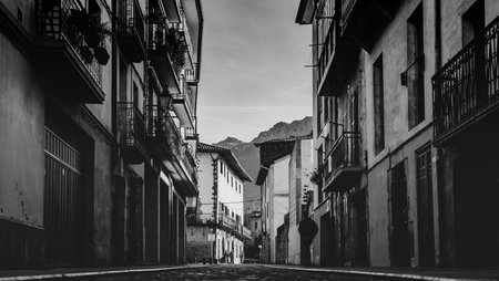 Quiet European old town street with historic residential buildings and balconies. Black and white perspective with distant mountains. Timeless urban architecture. Travel and heritage concept.の写真素材