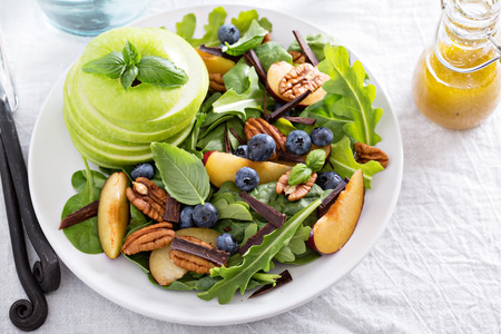 Fresh healthy salad with leafy greens, plums, nuts and appleの写真素材