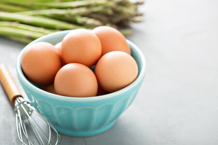 Fresh eggs in a bowl with a whisk and asparagus in background