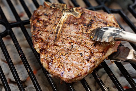 Tbone beef steak being cooked on a grill with tongsの写真素材