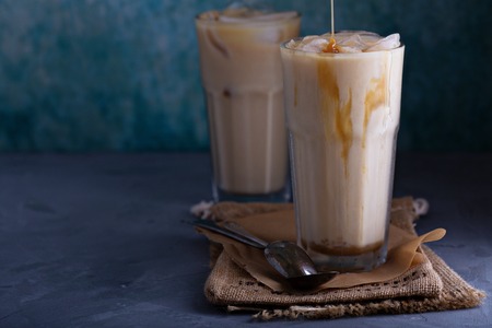 Iced coffee with milk in tall glasses on the table with caramel syrup poured overの写真素材