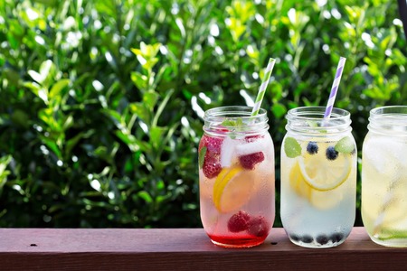 Variety of lemonade in mason jars with berries and fruits on the front porchの写真素材