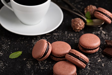 Chocolate french macarons with ganache filling on a black table with coffee