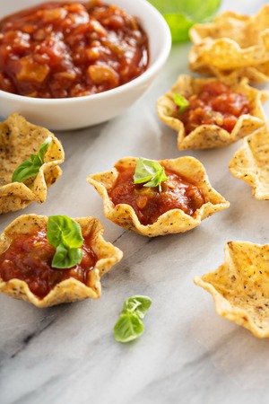 Small mexican style appetizers made with tortilla bowls and tomato salsa on marble board