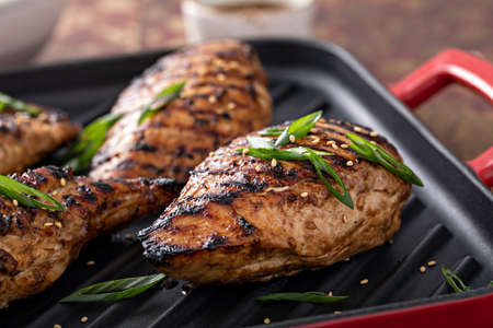 Grilled teriyaki chicken breast on a grill pan with green onions